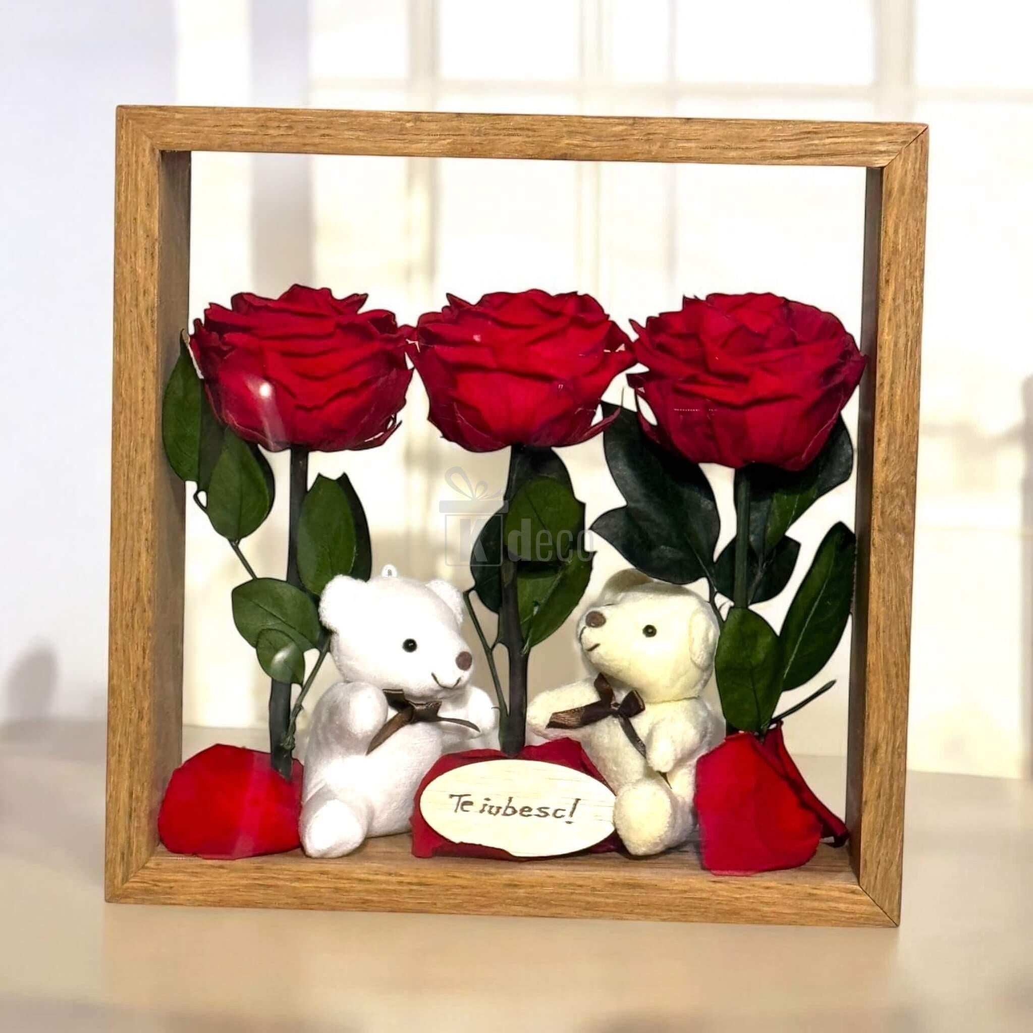 Decor floral cu trandafiri criogenați roșii și doi ursuleți de plus, în ramă de lemn, ideal pentru ocazii romantice și cadouri de dragoste.